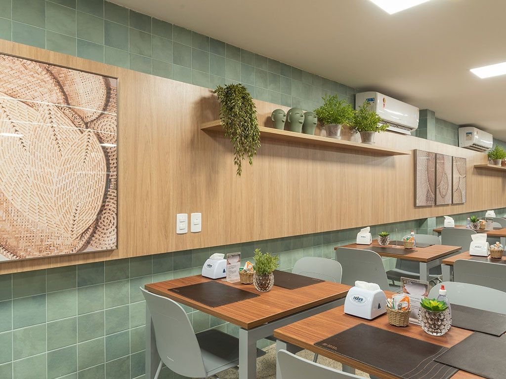 Interior do restaurante com mesas, cadeiras, painéis de madeira e vegetação. Parede de azulejos verdes.