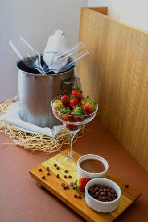 Balde de champanhe com taças, morangos, molho de chocolate e grãos de café sobre uma tábua de madeira.