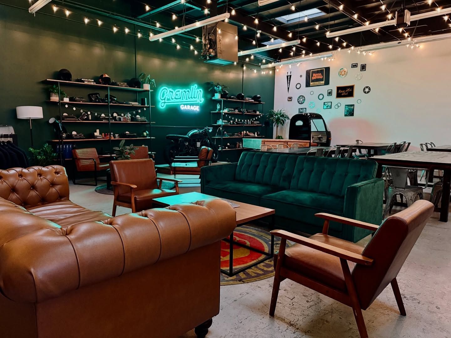 A lounge area featuring a brown leather sofa, a green velvet sofa, and armchairs under string lights in a rustic studio.