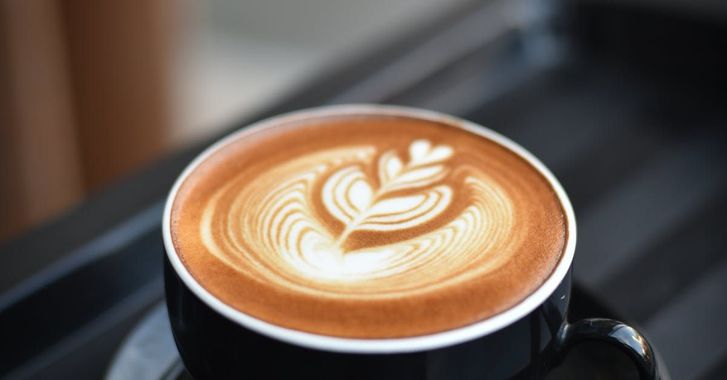 A close up of a cup of cappuccino with a leaf design on the foam.