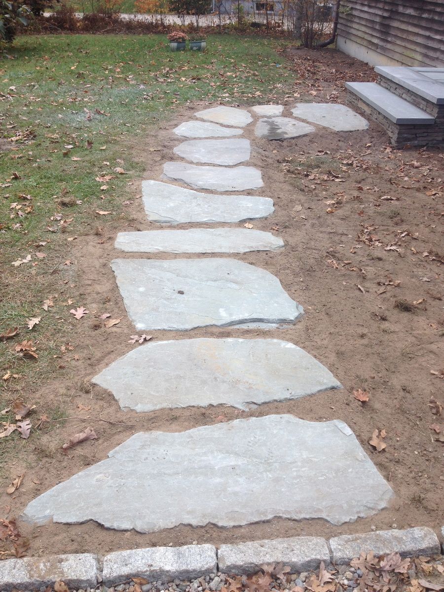 A stone walkway leading to a house in a yard