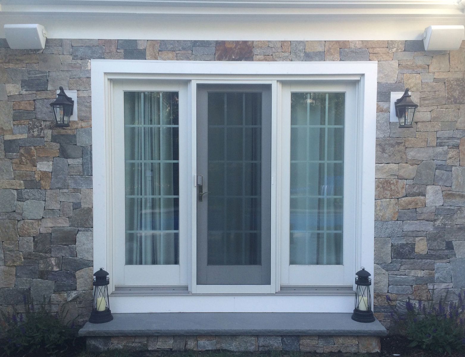 A stone wall with a sliding glass door and two lanterns on the porch