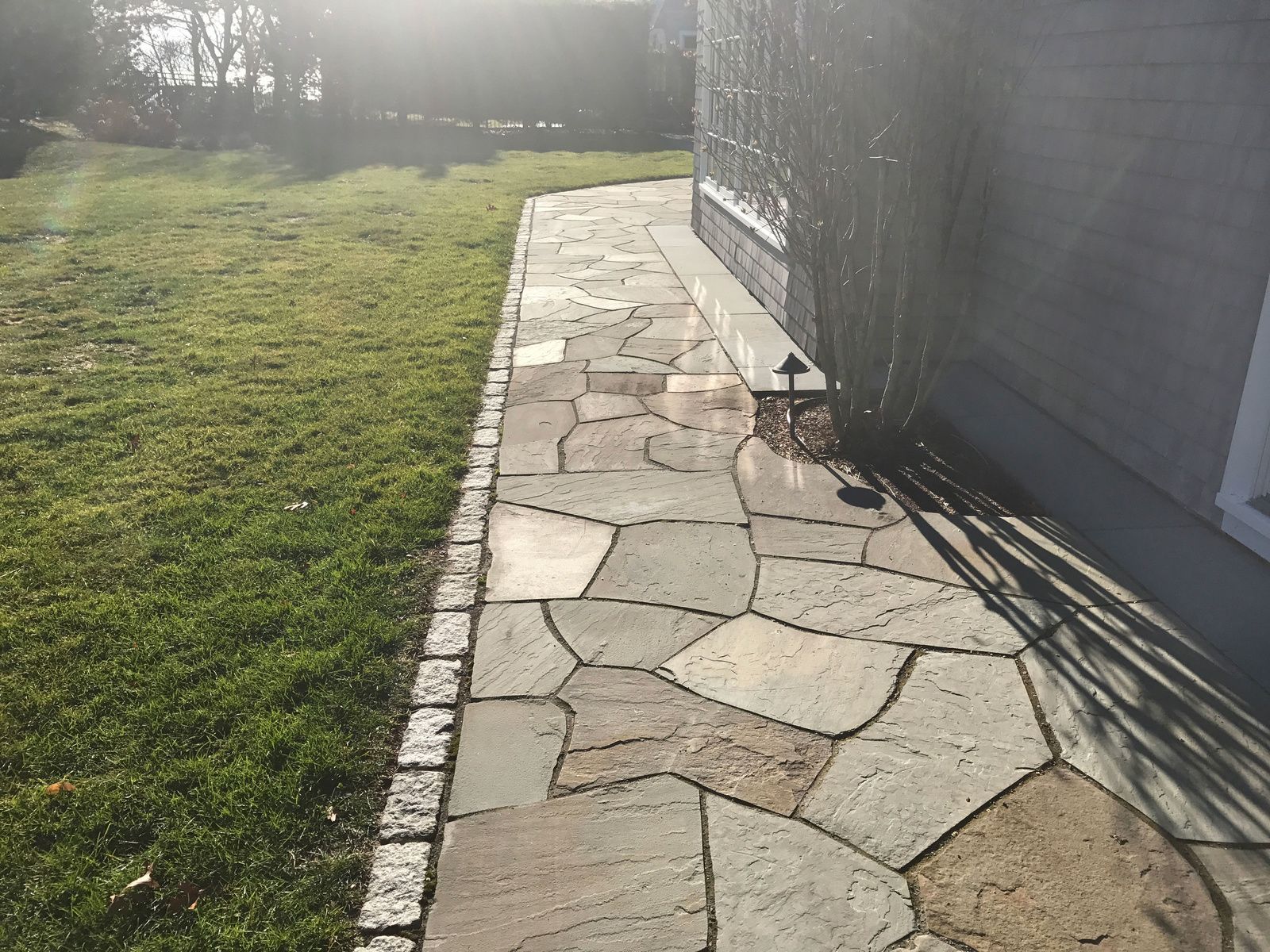 A stone walkway leading to a house next to a lush green lawn