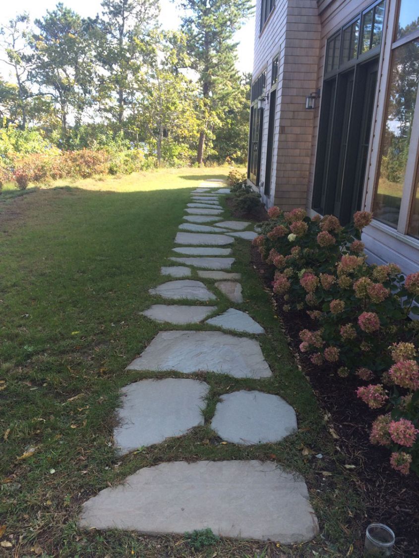 A stone walkway leading to a house with flowers on the side