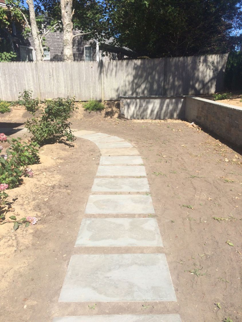 A stone walkway leading to a house with a fence in the background