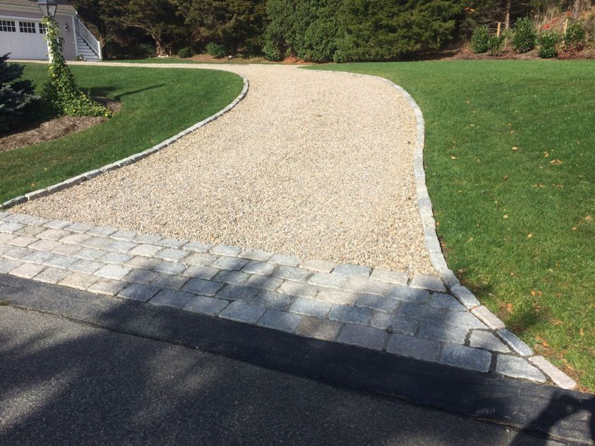 A gravel driveway leading to a house with a lush green lawn