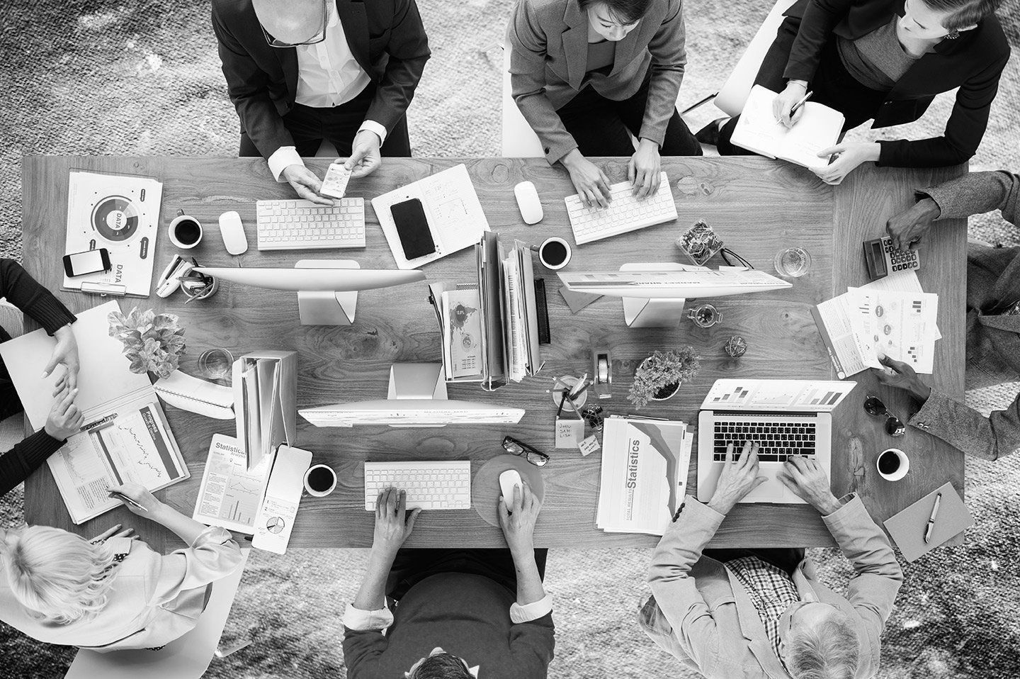 A group of people are sitting around a table with laptops and papers.