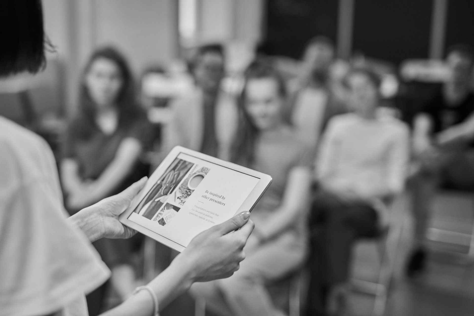 A woman is holding a tablet in front of a group of people.