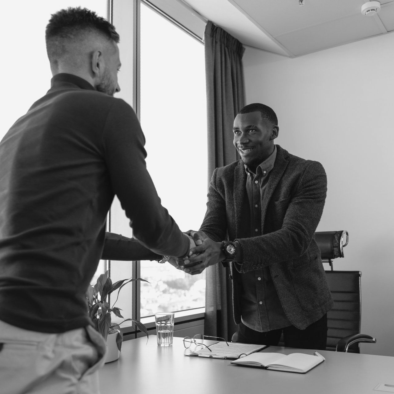 Two men shaking hands in front of a window in a black and white photo