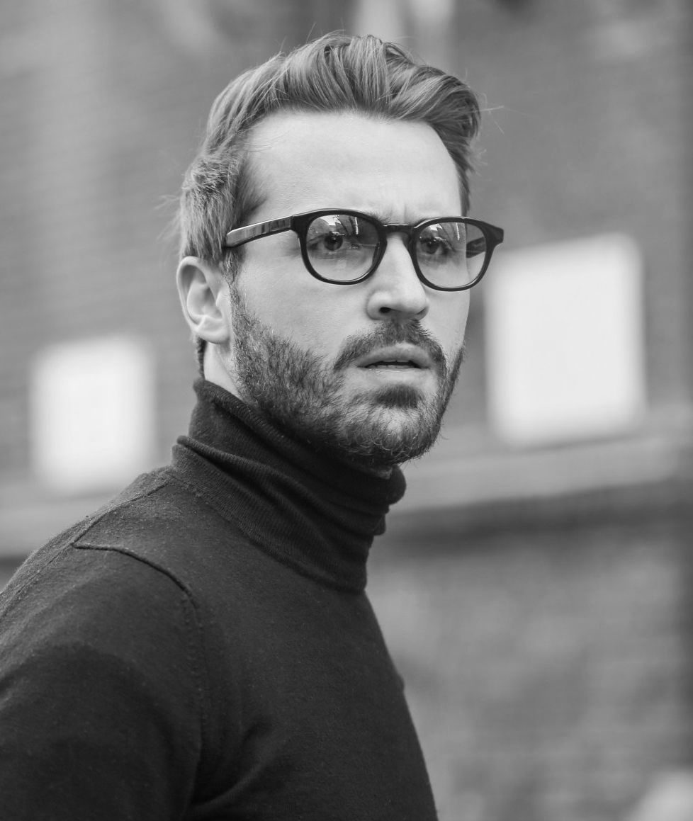 A man with a beard and glasses is wearing a black turtleneck and glasses.