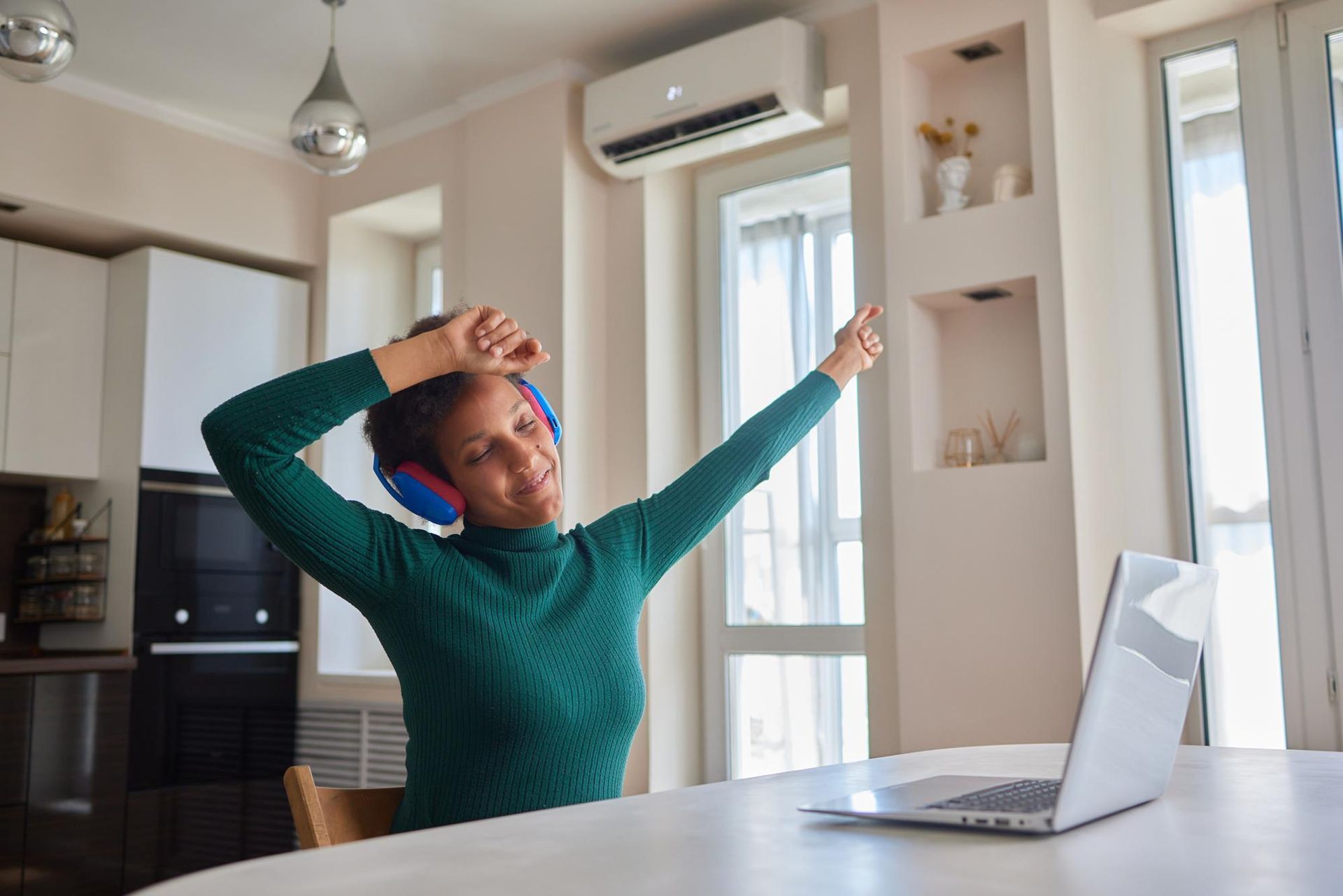 A woman wearing headphones is sitting at a table with a laptop.