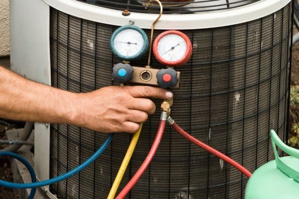 A man is working on an air conditioner with a hose attached to it.