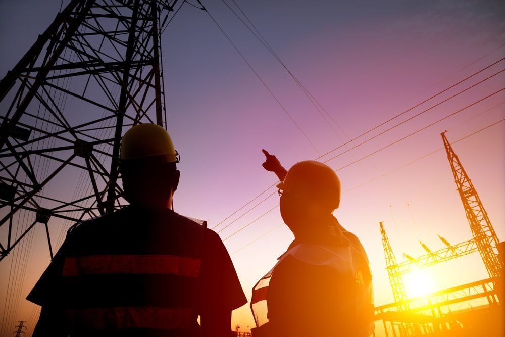 Two Workers Watching The Power Tower and Substation With Sunset In The Background — Barnes Electrical in Mackay, QLD