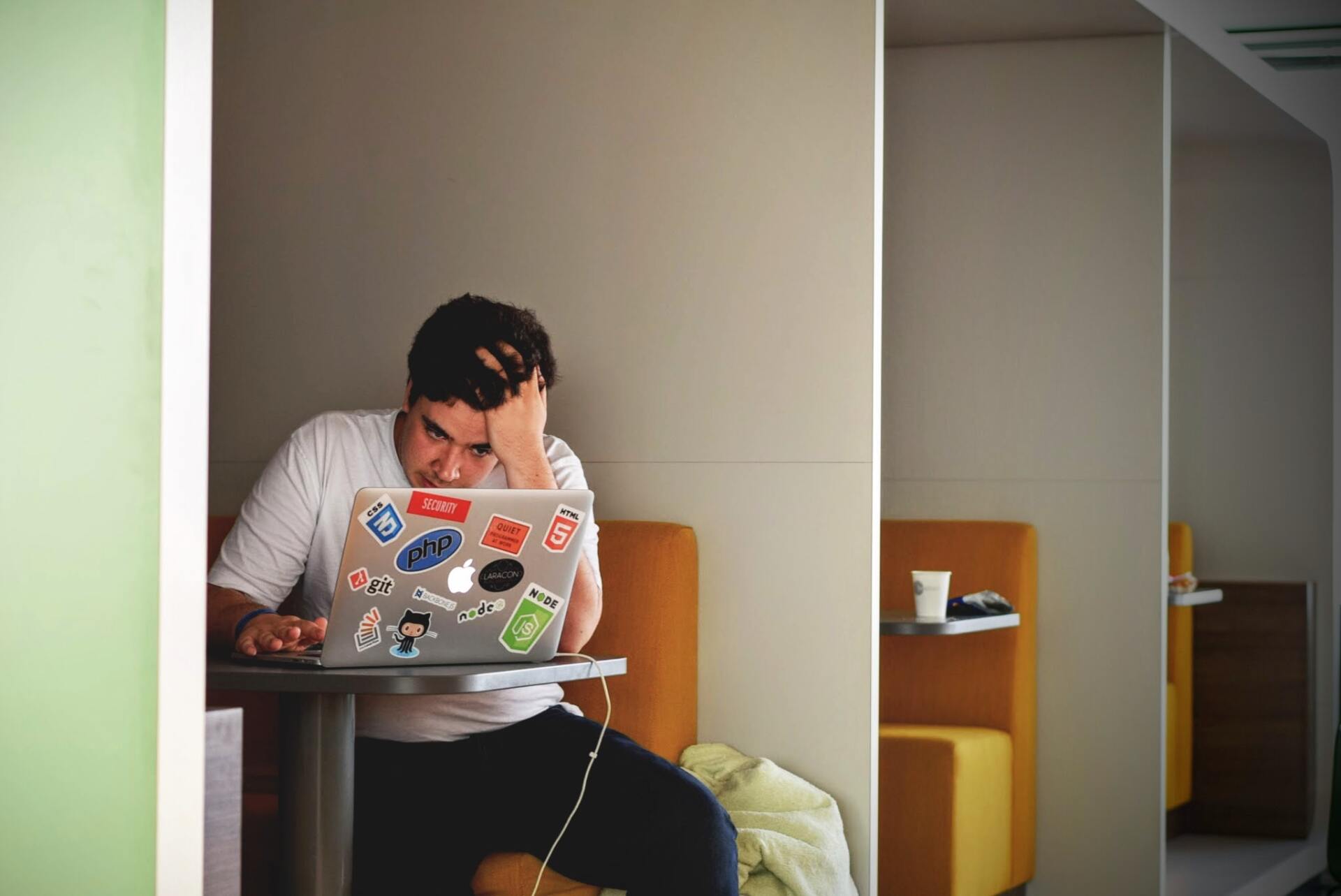 A man in a white t-shirt looking at a computer, stressed.
