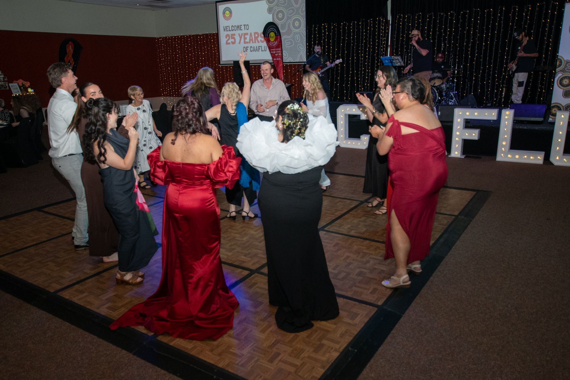 People dancing on a lit dance floor at an event. Stage with band and lights in the background.