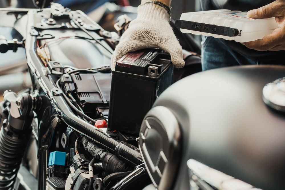A Gloved Hand Places a Black Motorcycle Battery — Deri's Mobile Mechanical In Parap, NT