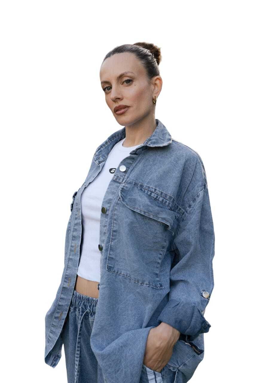 Mujer con chaqueta vaquera, top blanco y pantalones, mirando a la cámara.