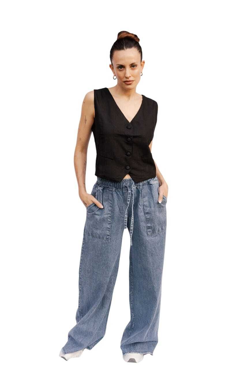 Mujer con chaleco negro y pantalones vaqueros holgados, manos en los bolsillos, mirando hacia delante.