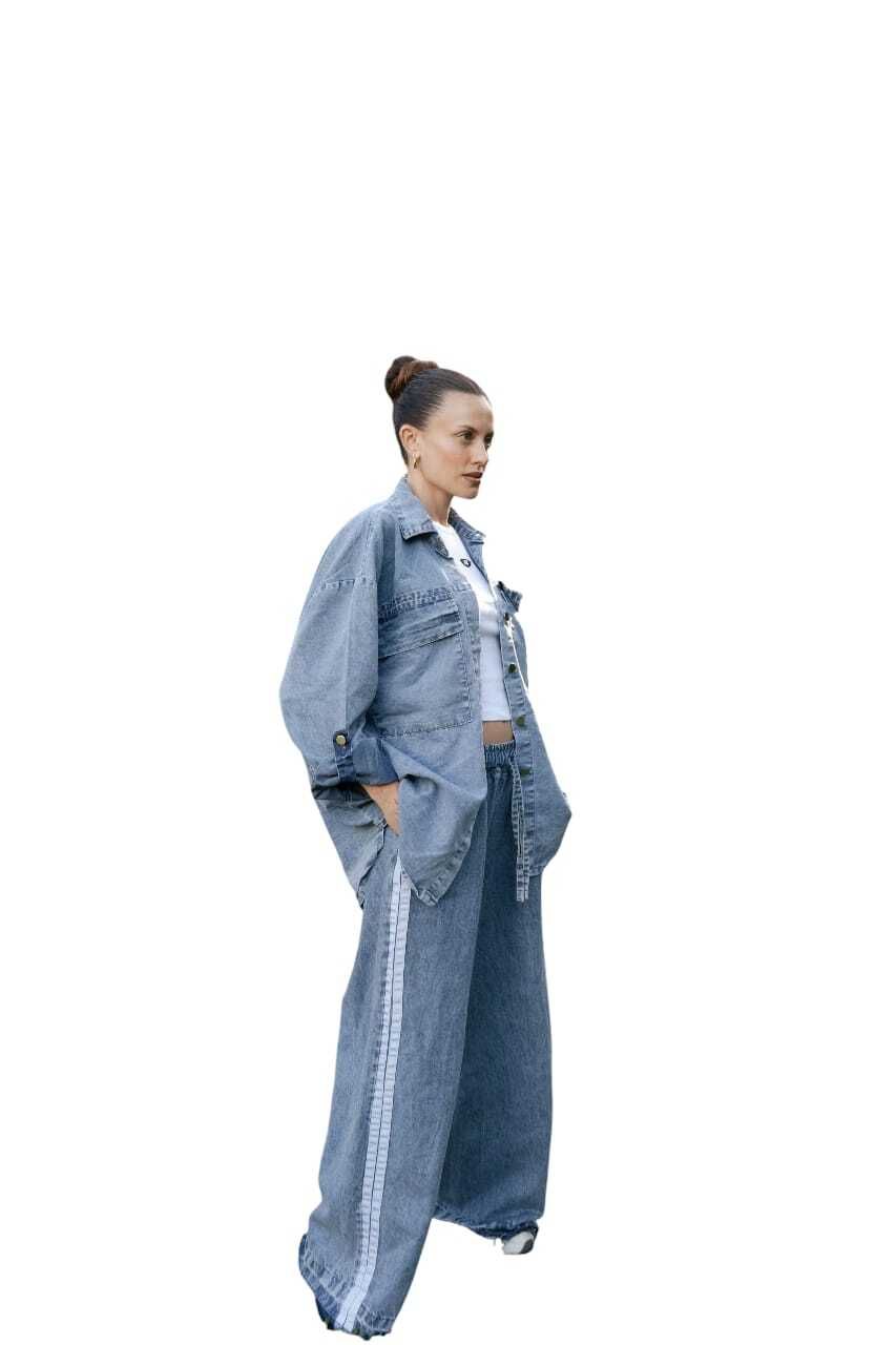 Mujer con chaqueta y pantalones vaqueros, mirando hacia un lado. Conjunto azul claro, manos en los bolsillos.