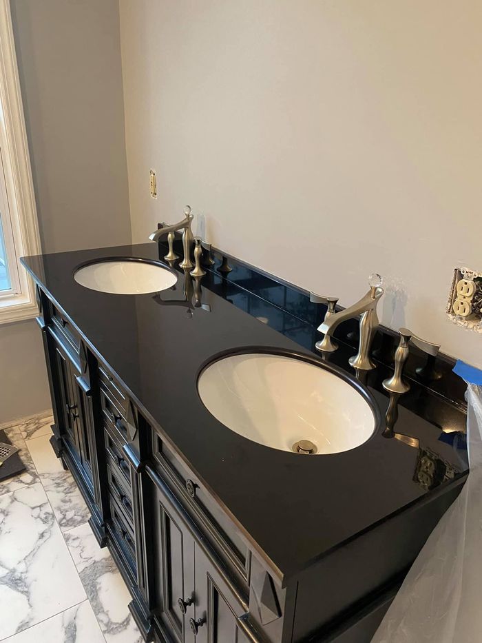 A bathroom with two sinks and faucets on a black counter top.