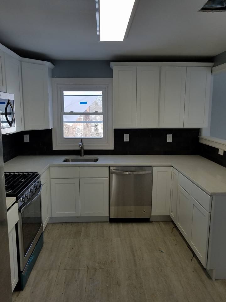 A kitchen with white cabinets , stainless steel appliances and a window.