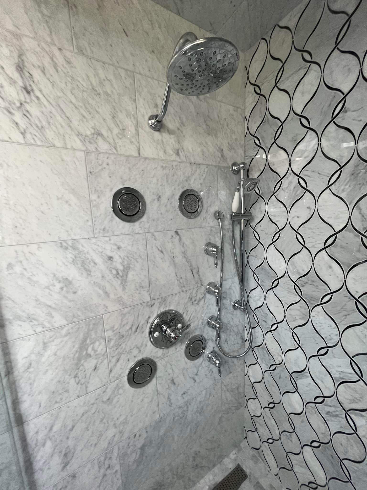 A shower with a marble wall and a chrome shower head.