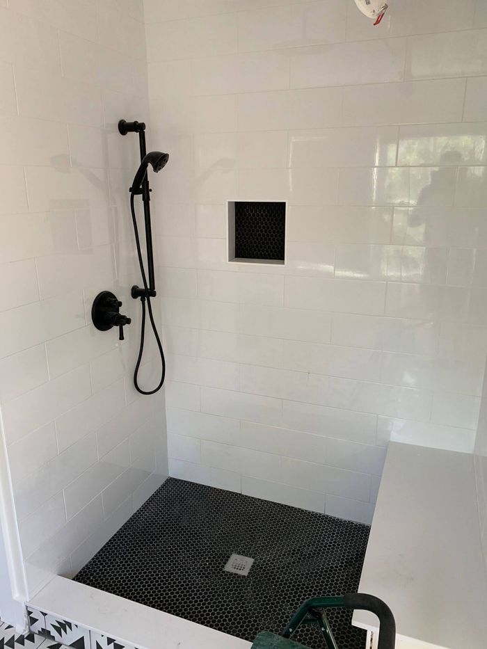 A bathroom with white tiles and a black shower head.