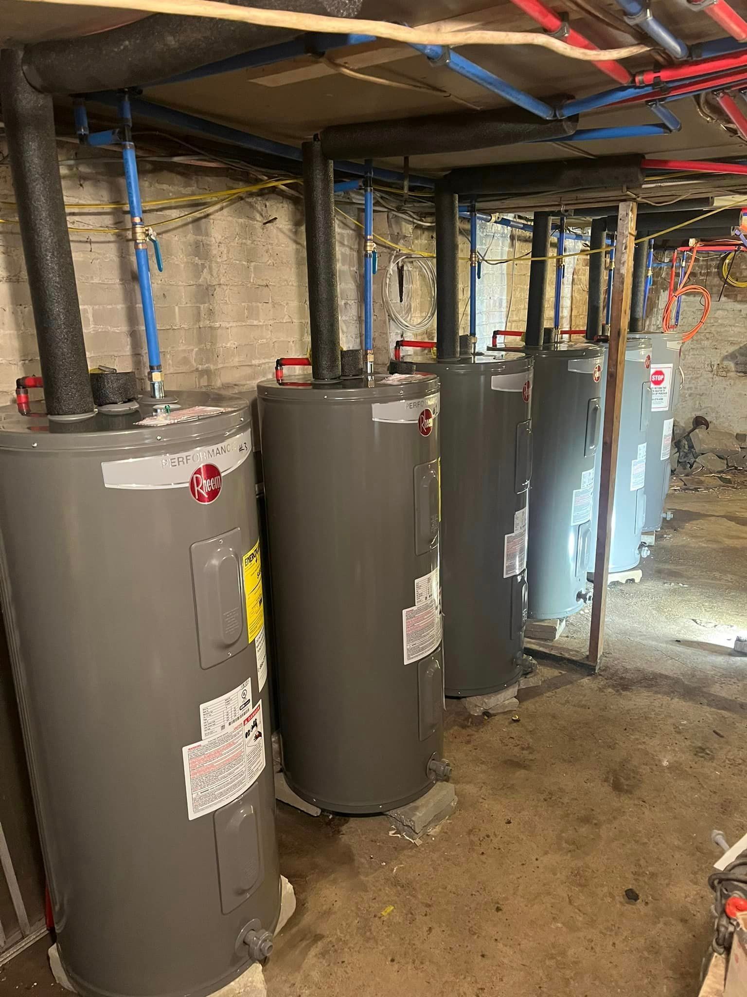 A row of water heaters are sitting next to each other in a basement.