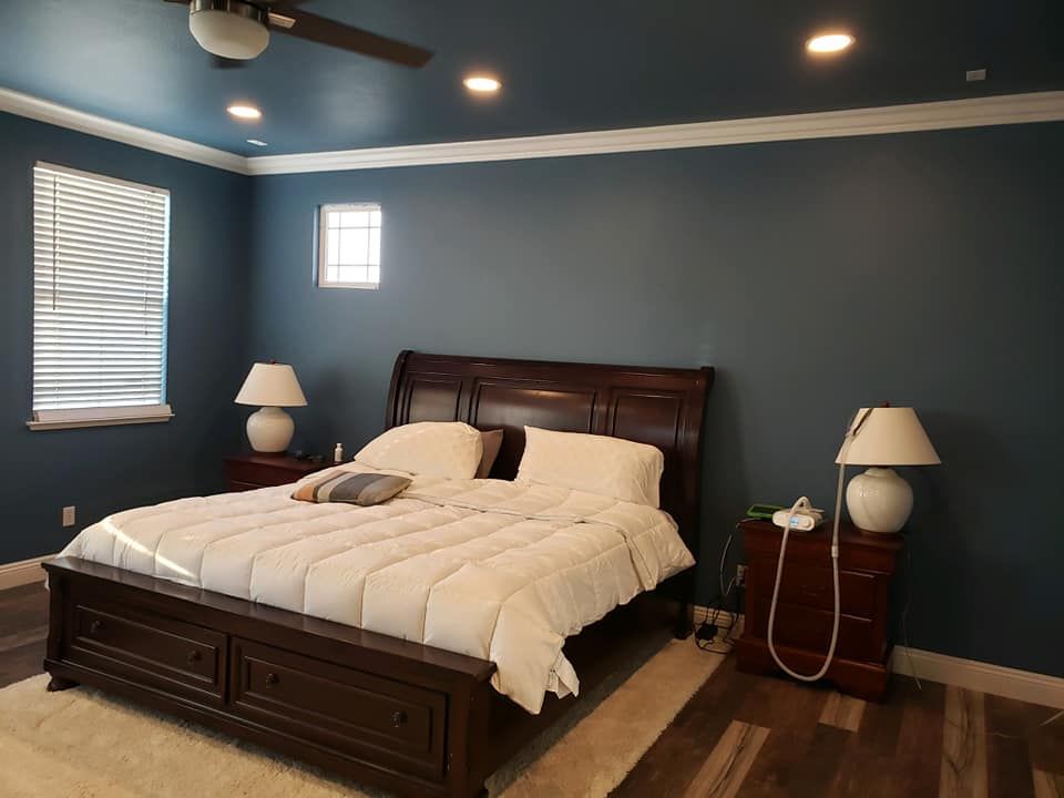 Bedroom with blue walls, dark wood bed and furniture, white bedding, two lamps, and a window.