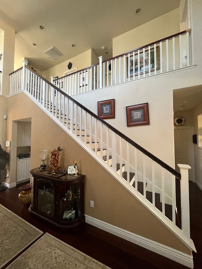 Two-story interior with a staircase, white railing, dark wood accents, and a small cabinet.