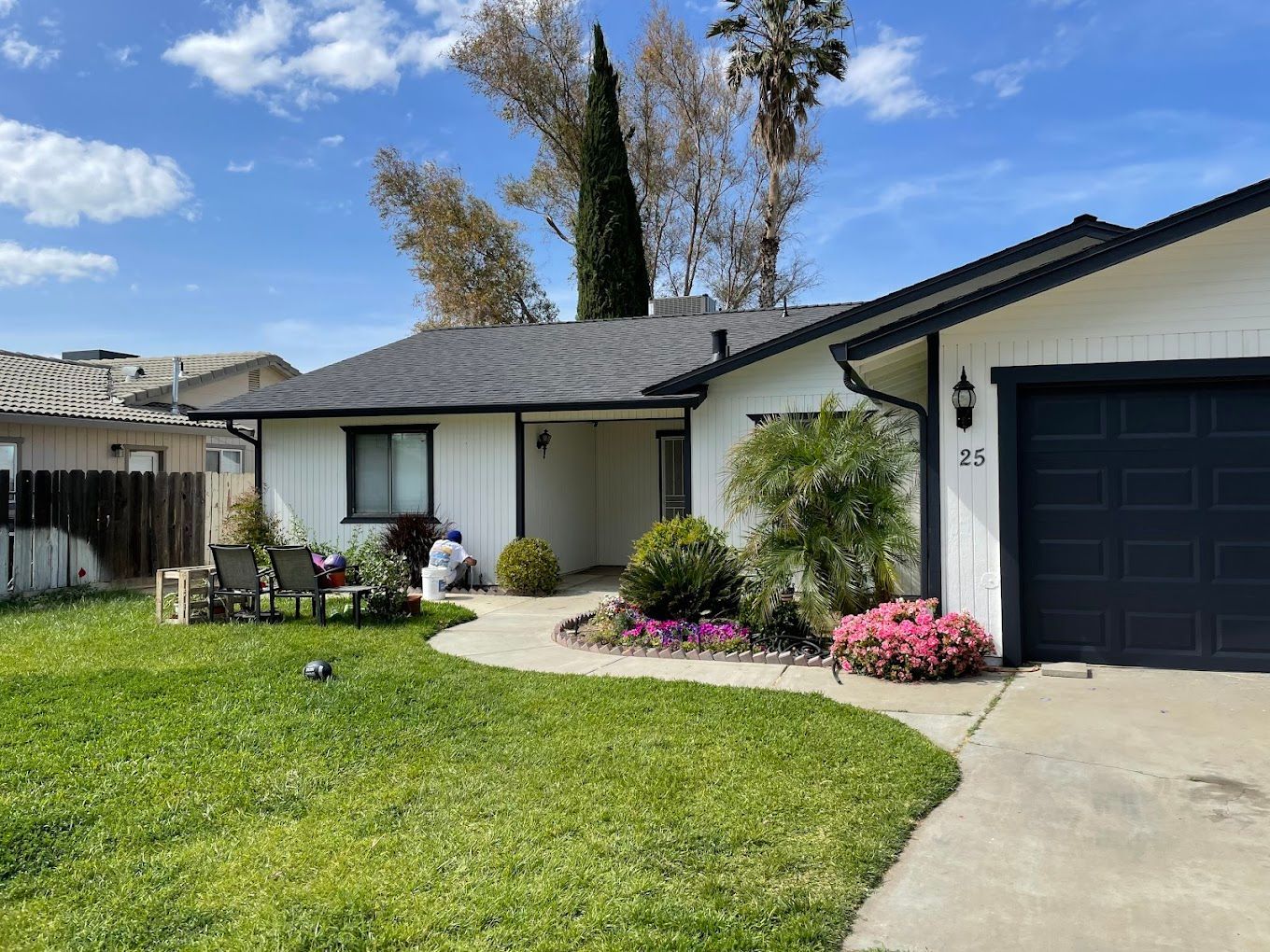 White house with black trim, a dark garage door, green lawn, and a winding path leading to the entrance.