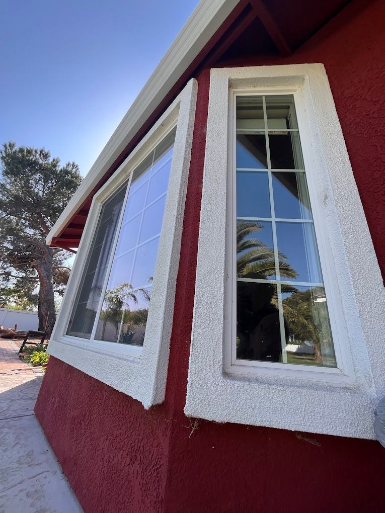 Red building corner with two white-framed windows, against a blue sky, outside.