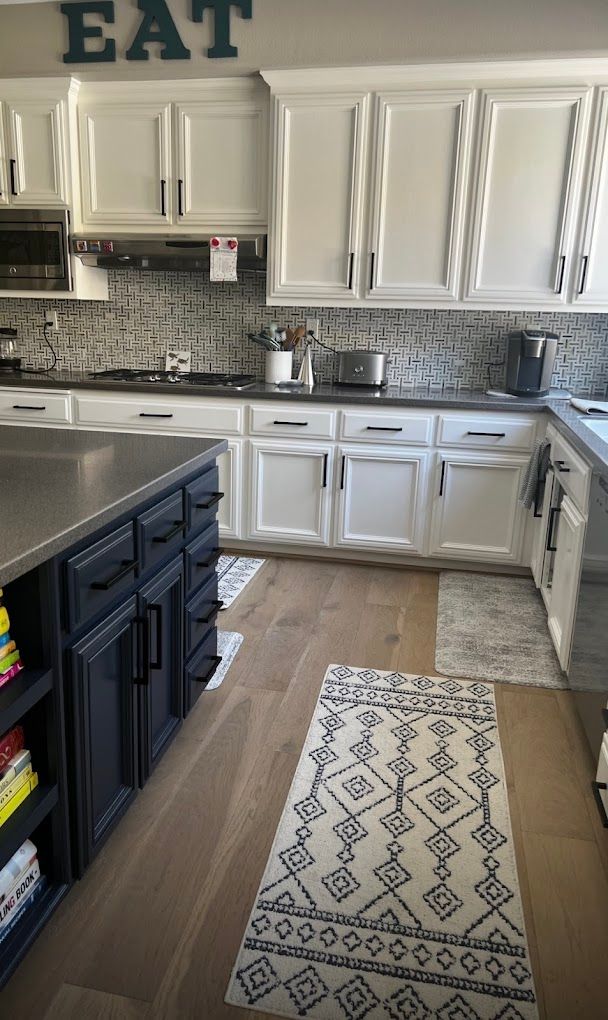 Kitchen with white cabinets, dark island, and patterned rugs on wood floor.
