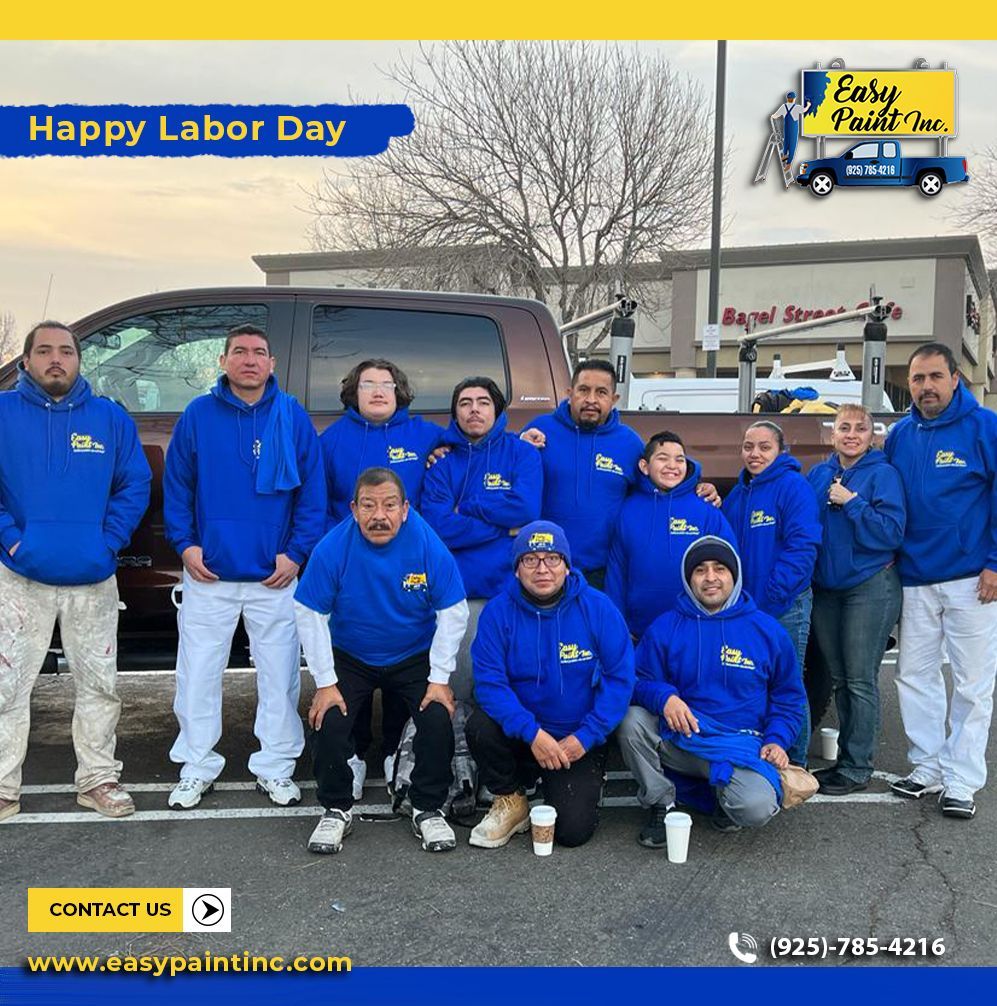 A group of painters in blue hoodies pose for a photo in front of a truck, celebrating Labor Day.