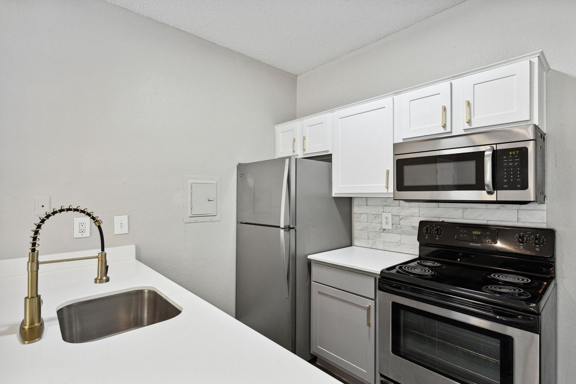 Small, modern kitchen with white cabinets, stainless steel appliances, and a white countertop.