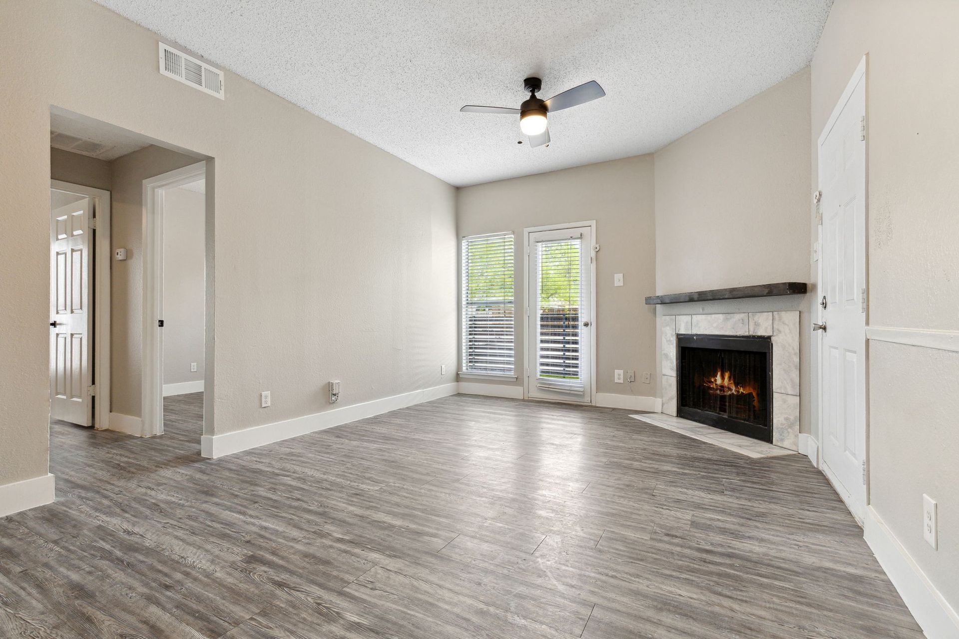 Empty living room with gray wood-look flooring, fireplace, and French doors leading to a balcony.