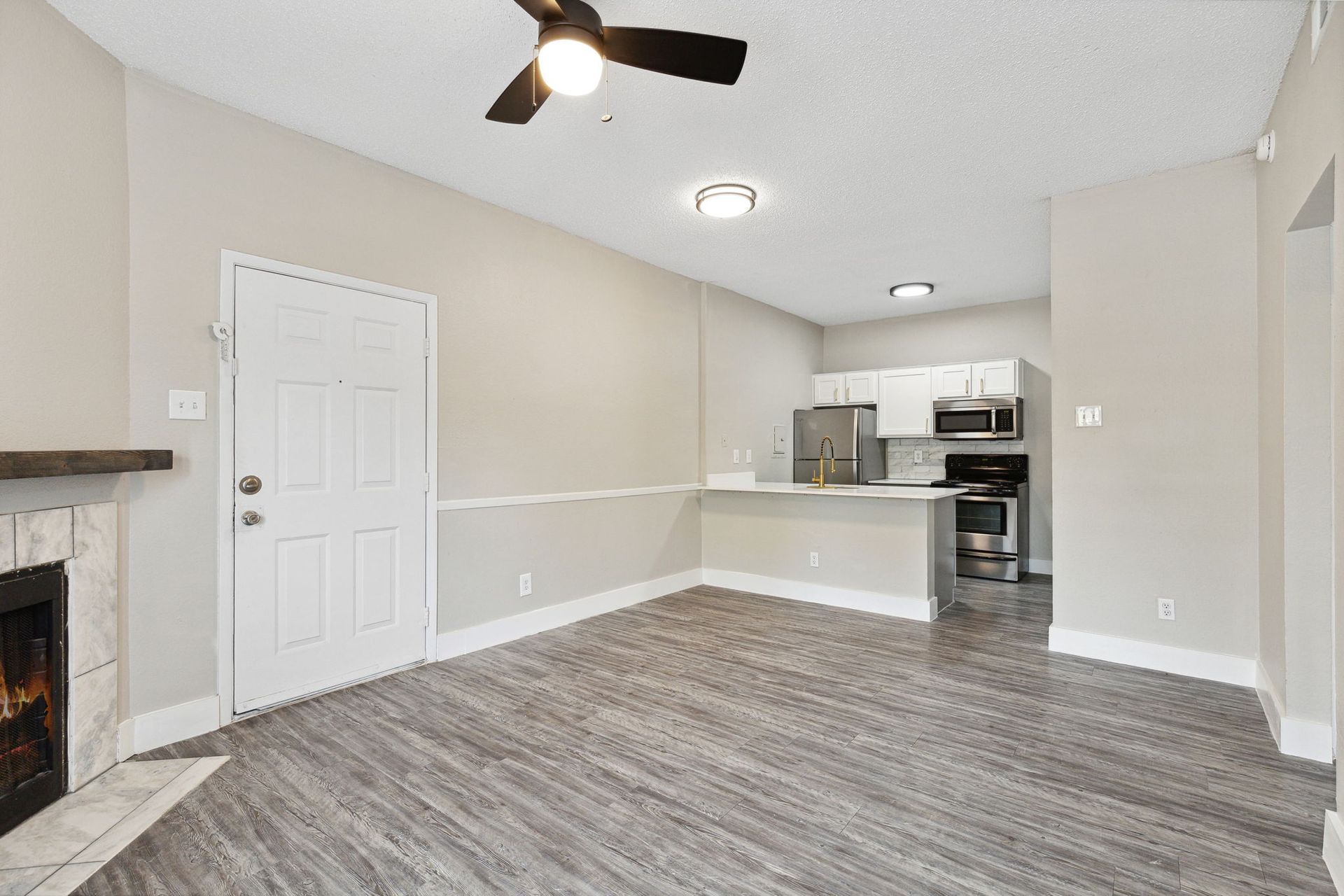 Empty living room with a fireplace and open kitchen; gray walls and flooring.