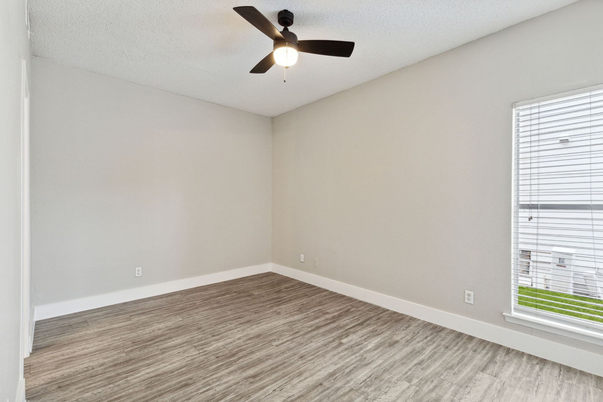 Empty room with gray walls, wood-look flooring, and a ceiling fan. Window on the right.