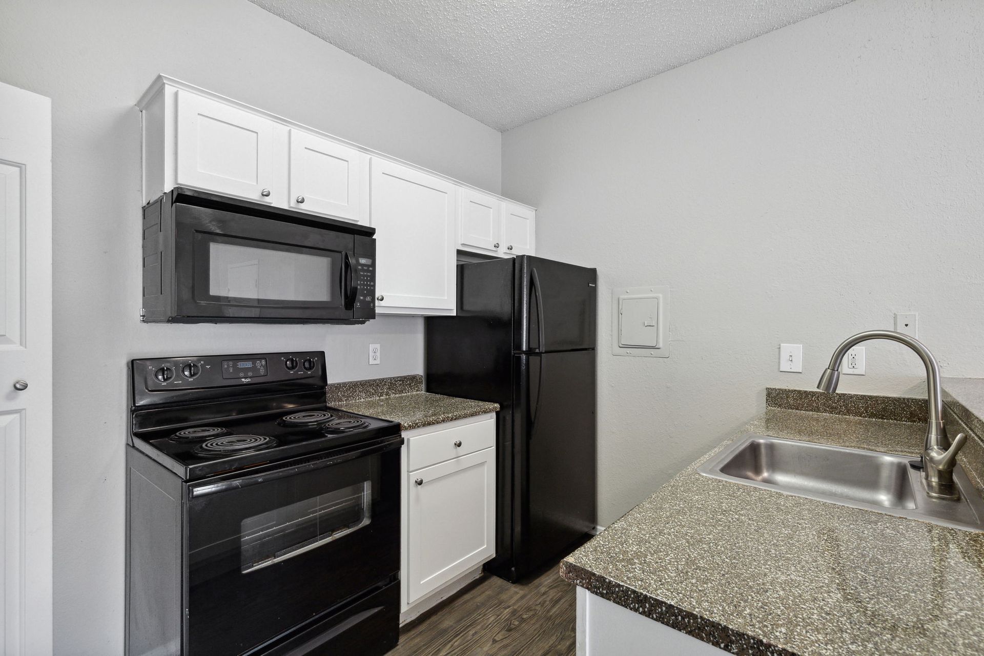 Small kitchen with black appliances, white cabinets, and speckled countertop.