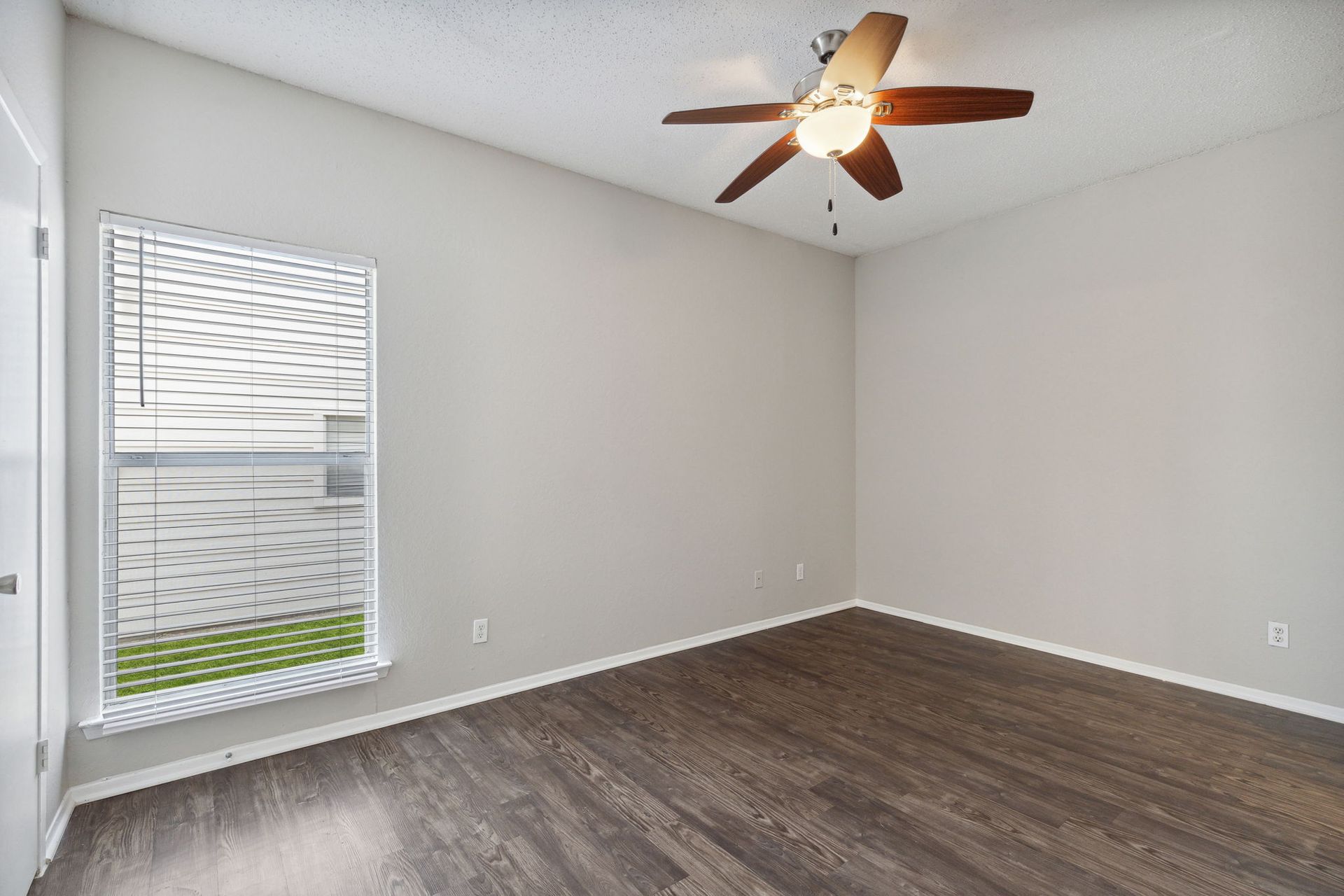 Empty room with wood-look flooring, neutral walls, window with blinds, and ceiling fan.
