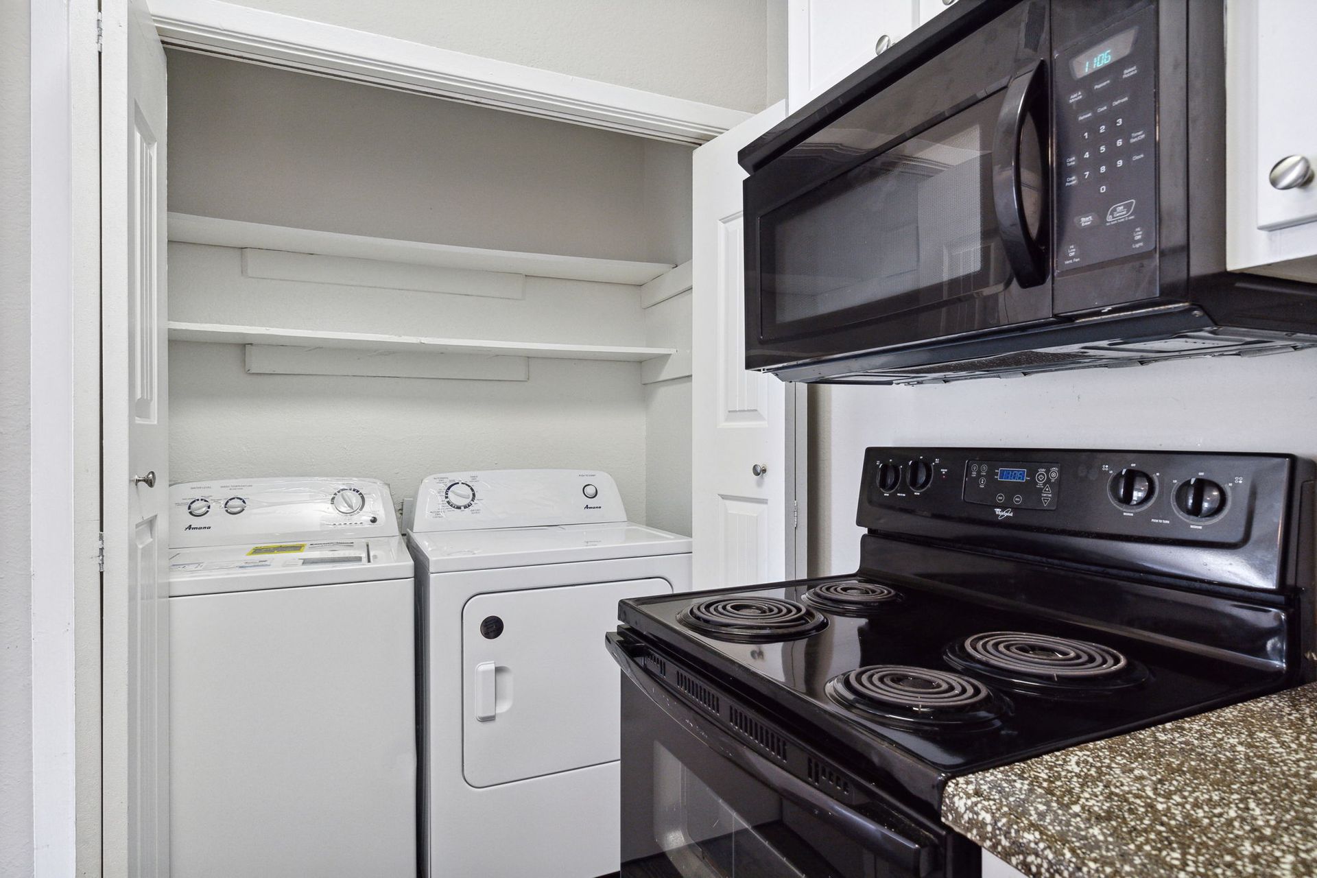Laundry closet with washer and dryer, next to a black stovetop and microwave.