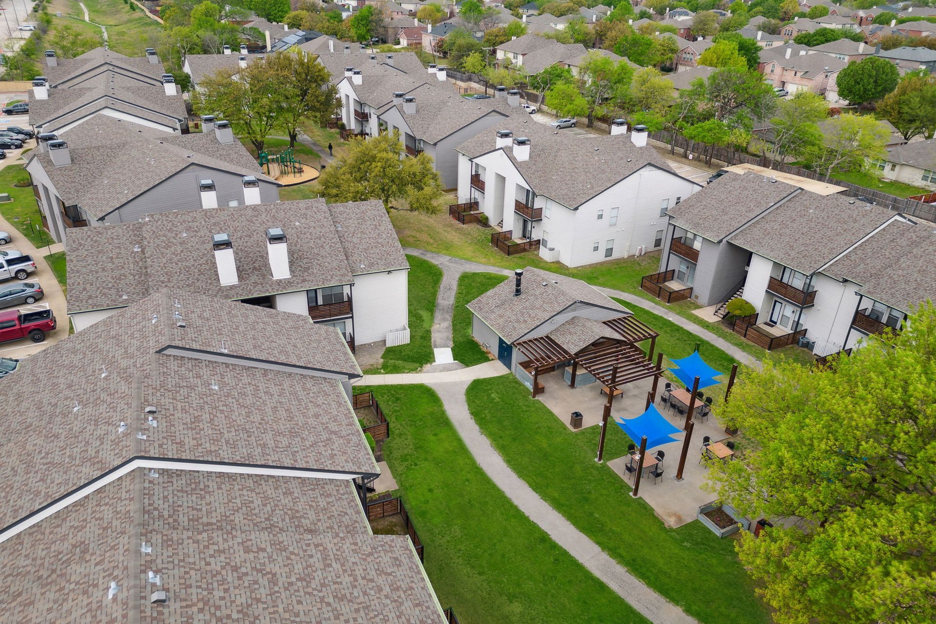 Aerial view of apartment complex with green spaces, playground, and cars.