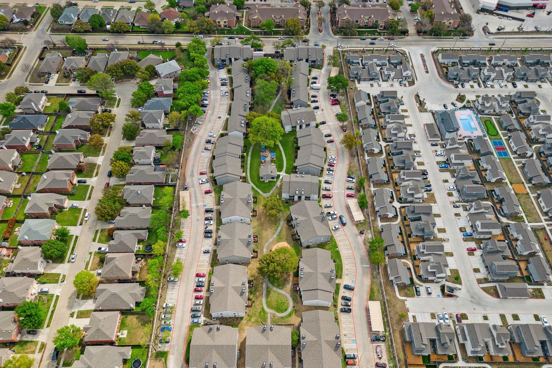 Aerial view of residential area with houses, roads, trees, and a swimming pool.