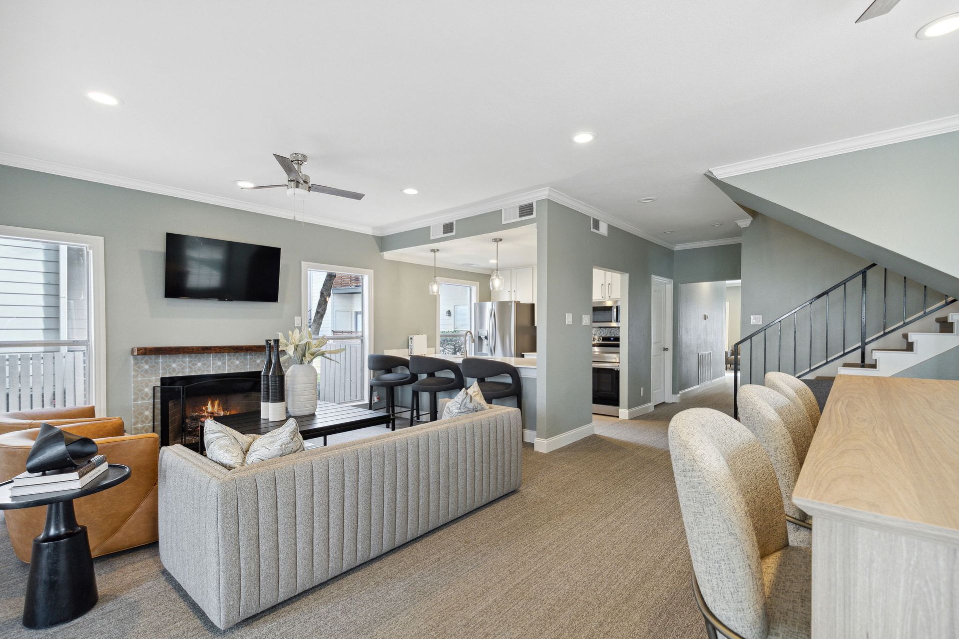 Fireplace, stairs, and kitchen access. Light gray walls, neutral furniture, and carpet.