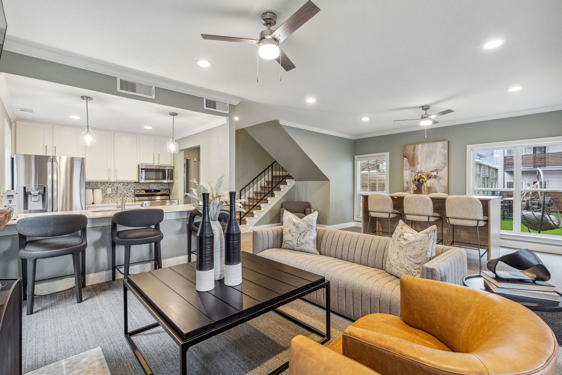 Open-concept living space with a kitchen, living area, bar, and stairs. Neutral colors, modern decor, and natural light.