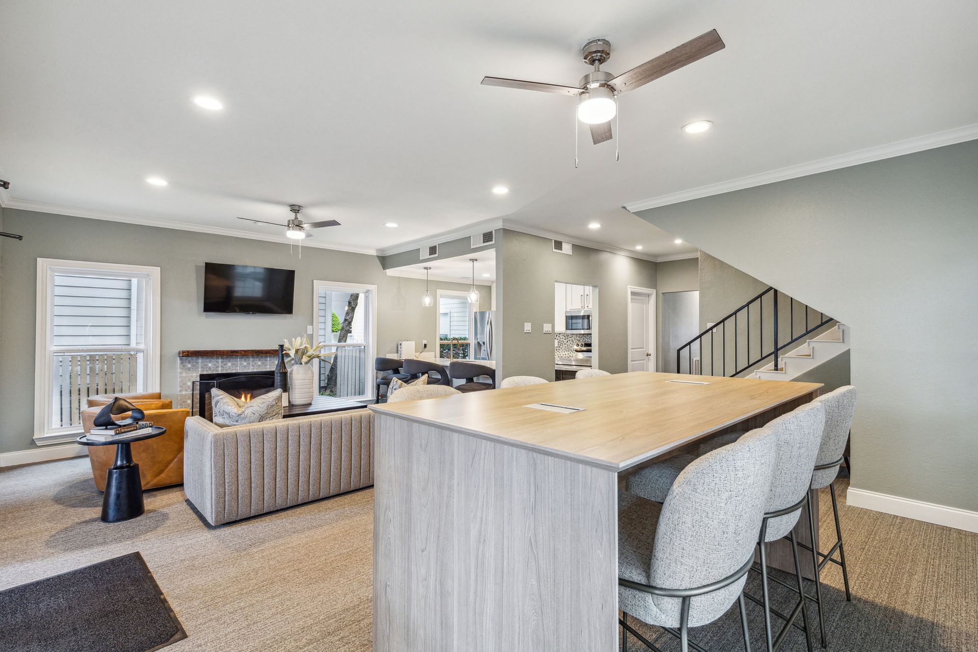 Island seating, sofa, TV, and stairs. Gray walls, light wood tones, and beige carpet.