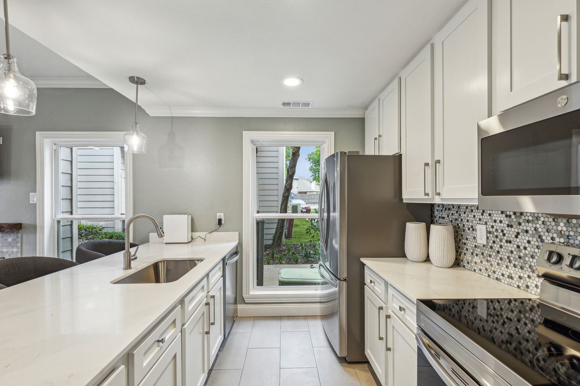 Modern kitchen with white cabinets, stainless steel appliances, and a long countertop.