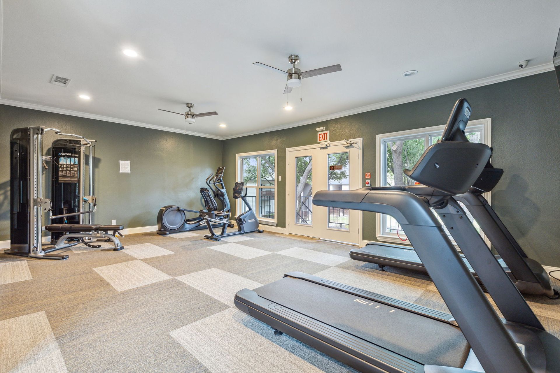 Gym with exercise equipment: treadmill, weight machine, recumbent bike, in a room with patterned carpet and green walls.