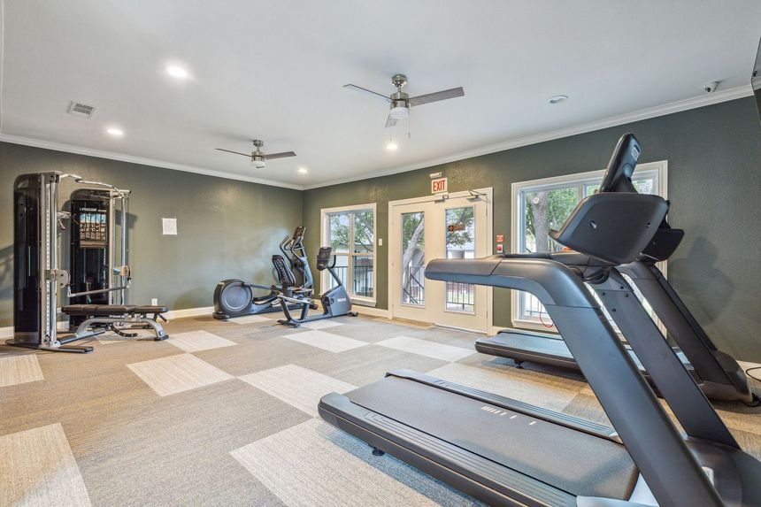 Gym with exercise equipment: treadmill, weight machine, recumbent bike, in a room with patterned carpet and green walls.