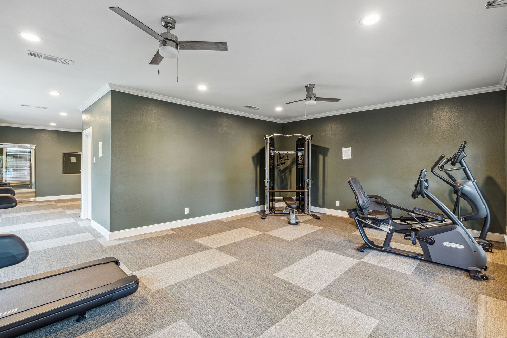 Gym with exercise equipment, gray and beige checkered floor, green walls.